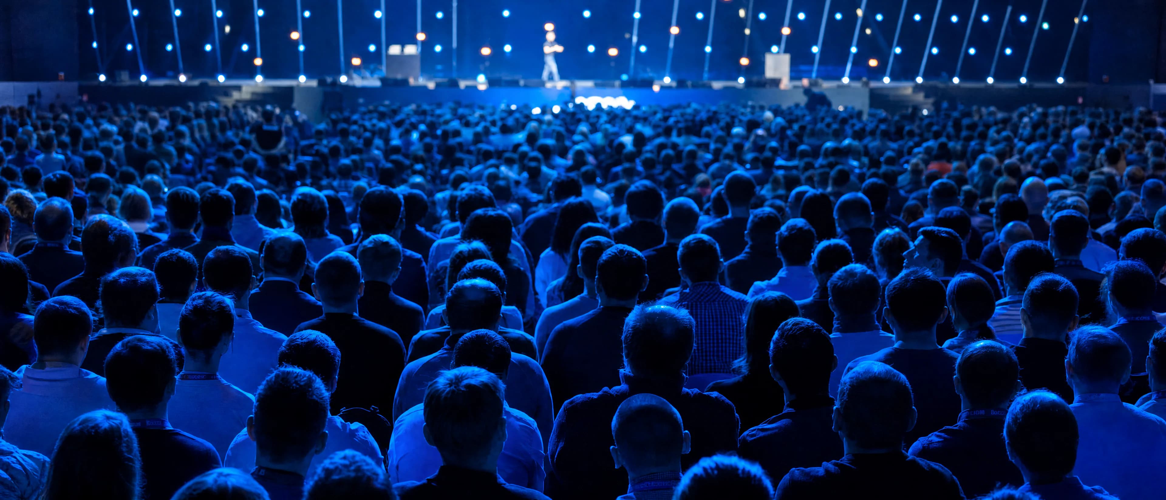 A conference hall, the audience seated, a speaker walking on stage